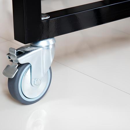 Close-up of a bolt caster wheel with a brake lever on a black metal frame on a glossy floor.