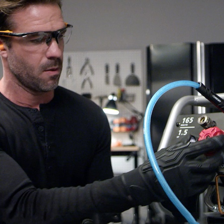 A man in safety glasses and gloves adjusting a valve on a black air compressor.