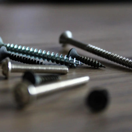 Close-up of various silver metal screws on a wooden surface.