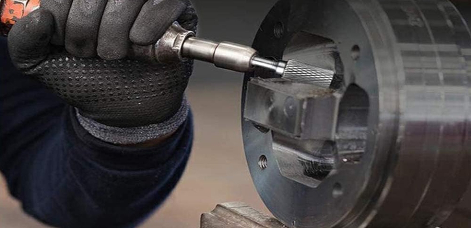 Worker using a die grinder with a single cut burr to machine a metal component.